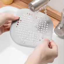 Person using a white colander under running water in a kitchen sink.